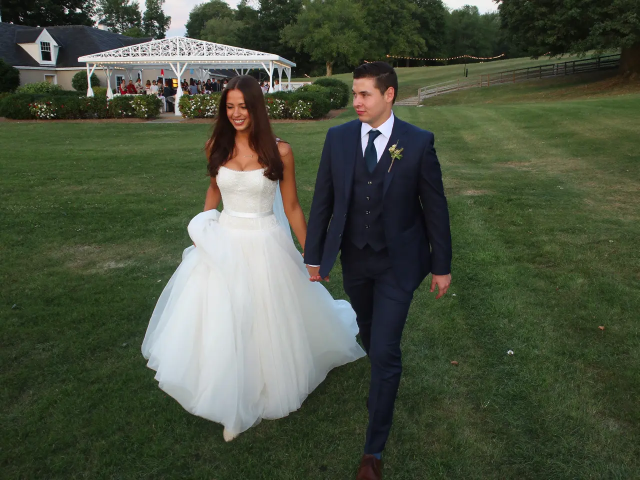 The couple walking hand in hand across the lawn