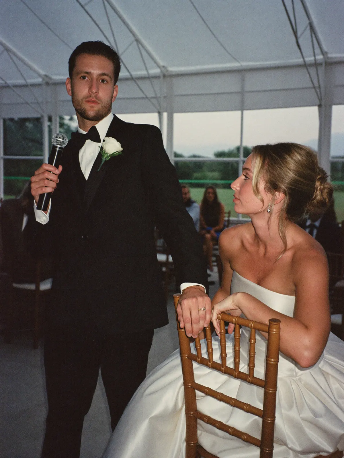 The groom mid-speech, looking down at his bride rather than at the room