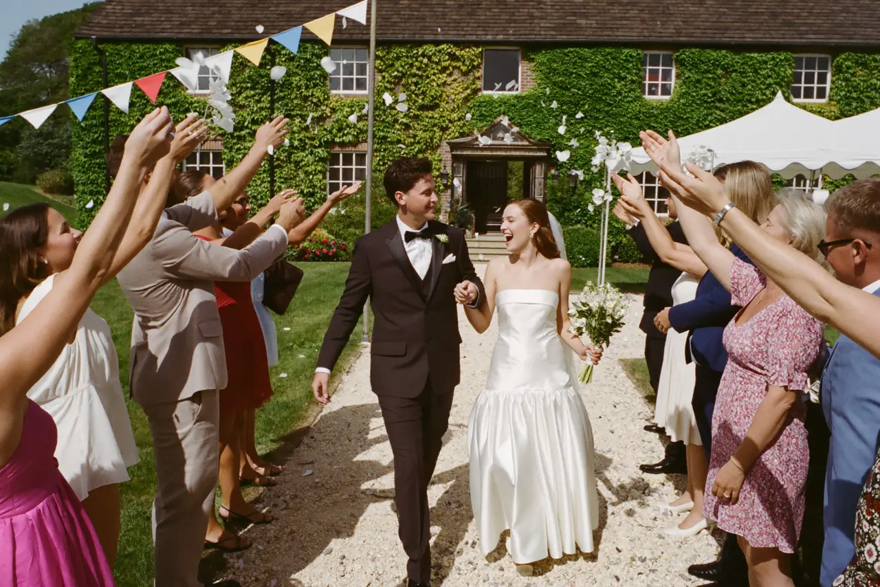 Guests throwing confetti over the laughing couple outside an English manor house